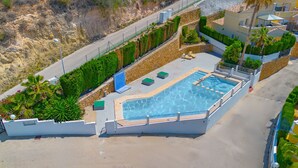 Vista aérea de una piscina con un muro de piedra, plantas verdes y un camino empedrado.