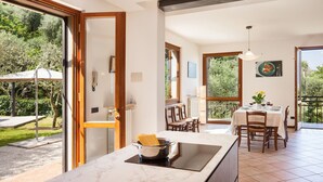 A modern kitchen with a marble countertop, a dining area with a table set for two, and a view of the garden through large windows. - Villa Carducci with lake view (Torri del Benaco)