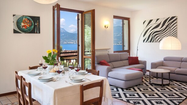A dining area with a table set for two, a sofa, and a patterned rug. - Villa Carducci with lake view (Torri del Benaco)