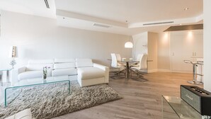 Ein modernes Wohnzimmer mit einem weißen Sofa, einem Glastisch und einem Essbereich mit einem Tisch und Stühlen.