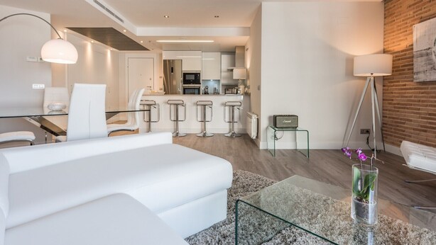 Ein modernes Wohnzimmer mit einem weißen Sofa, einem Glastisch und einer Bar mit Hockern.