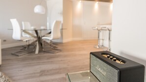 Ein modernes Wohnzimmer mit einem Glastisch, einem schwarzen Lautsprecher und einem Essbereich mit weißen Stühlen und einem Glastisch.