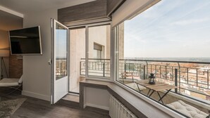 Eine moderne Wohnung mit großem Balkon, einem an der Wand befestigten Fernseher und Blick auf die Stadt.