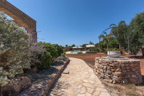 A stone pathway leading to a pool area, surrounded by lush greenery and a stone wall.
