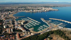 An aerial view of a coastal city with a marina, buildings, and a mountainous backdrop. - APARTMENT ALBATROS 1  3-2 (L'Escala)