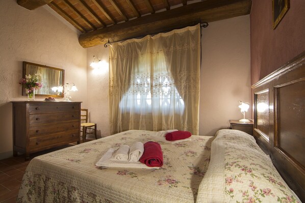 Une chambre à coucher avec un lit, une commode, un miroir et une fenêtre avec des rideaux.