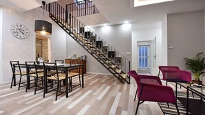 A modern living room with a staircase, a dining area with a wooden table and chairs, and a seating area with red chairs. - Apartment Tivoli Park, Ljubljana (Ljubljana)