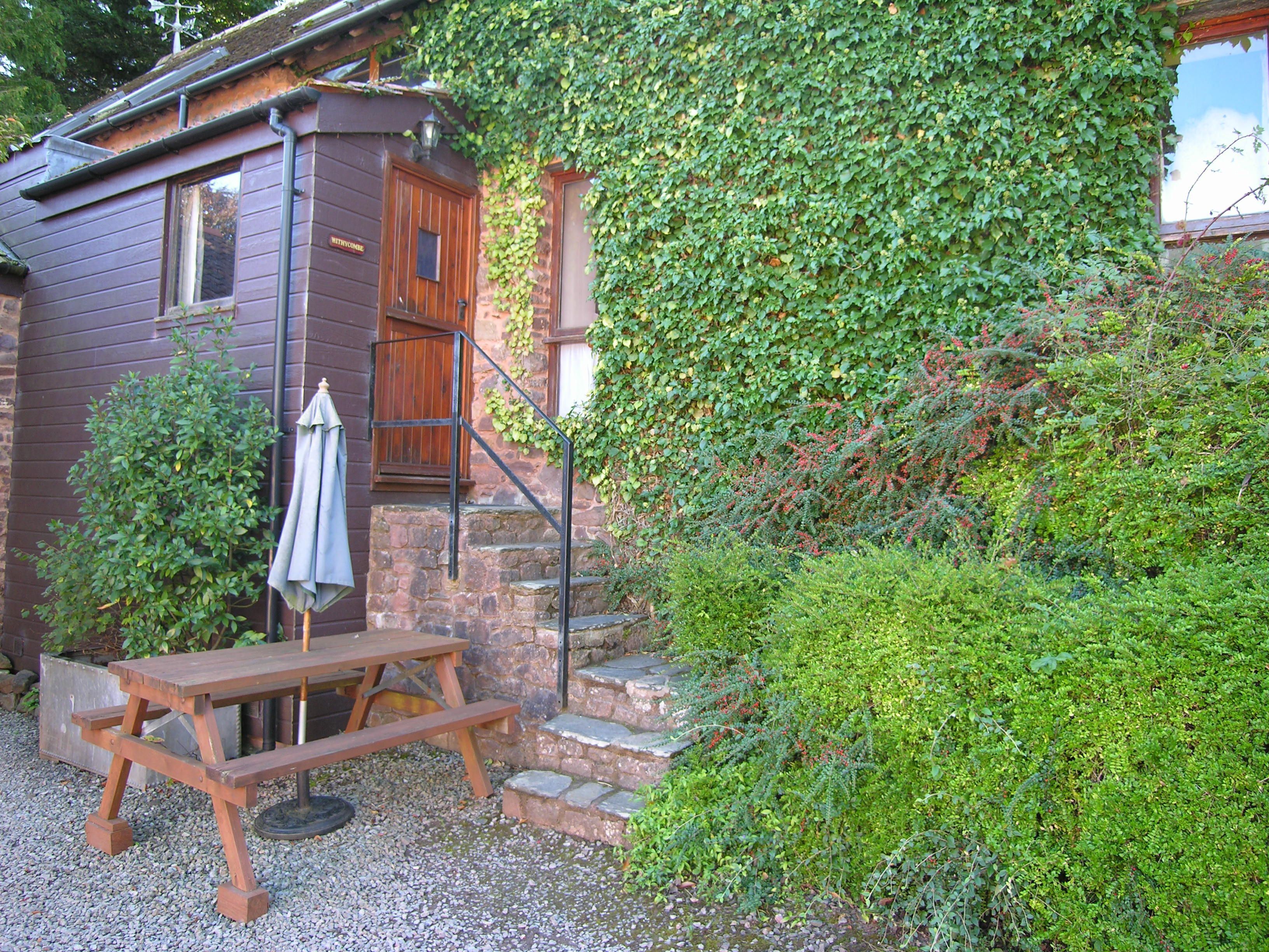 A rustic wooden cabin with a stone staircase, a wooden bench, and an umbrella.