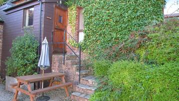 A rustic wooden cabin with a stone staircase, a wooden bench, and an umbrella.