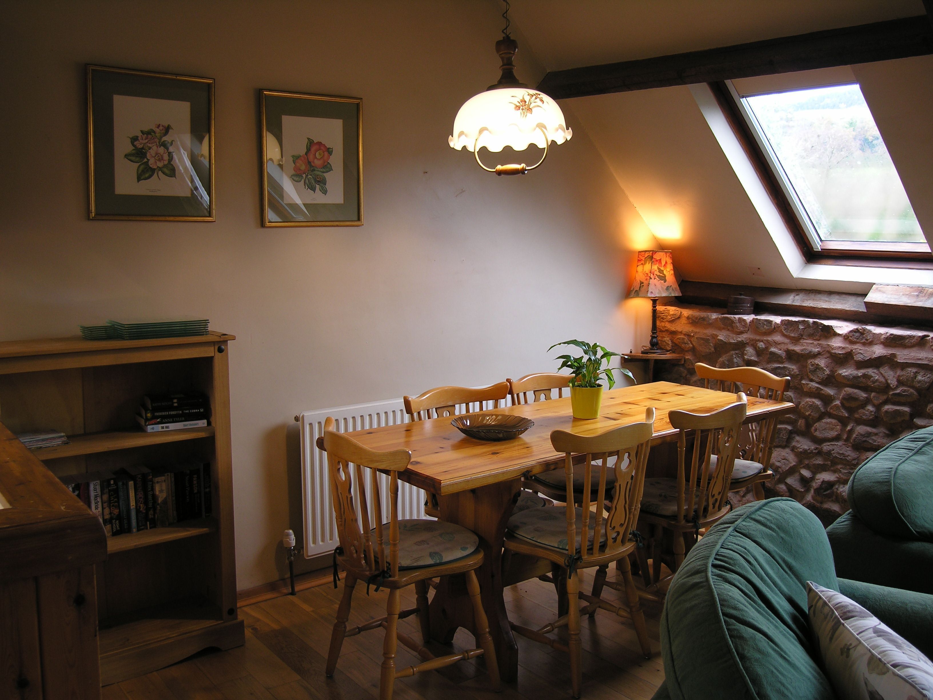 Un coin repas avec une table et des chaises en bois, une plante en pot, une bibliothèque et des œuvres d’art encadrées accrochées au mur.