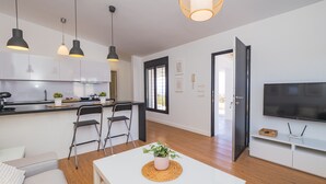 Een moderne keuken met witte kasten, een zwart aanrecht en een inbouwfornuis. Drie hanglampen, een potplant en een kleine tafel met stoelen.