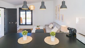 Een moderne woonkamer met een zwarte eettafel, twee potplanten, een grijze bank en een koffiezetapparaat.