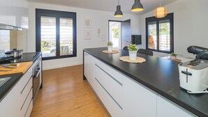 Een moderne keuken met een zwart aanrecht, witte kasten en een ingebouwde oven. Drie hanglampen hangen boven het aanrecht, en er staat een koffiezetapparaat aan de rechterkant.
