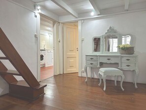 A room with a wooden staircase, a white dresser with drawers, a small stool, and a basket of flowers on the dresser.