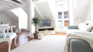 Un loft espacioso con techo alto, un televisor sobre un soporte de madera, un sofá gris y una silla blanca.