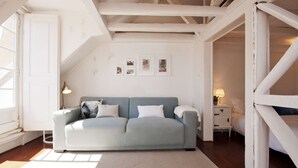 Una habitación con un sofá azul claro, una mesita de noche con lámpara y una pared decorada con cuadros.