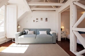 Une pièce avec un canapé bleu clair, une petite table de chevet avec une lampe et un mur orné de tableaux encadrés.