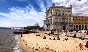 A beach with people and pigeons, a bridge in the background, and historic buildings. - ✨The Downtown Terrace: at Downtown with Fabulous Views, Sun Deck, Penthouse (Lisboa)