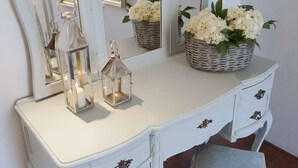 Un tocador blanco con dos faroles de cristal y una cesta de mimbre con flores blancas.