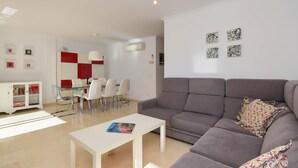 A modern living room with a grey sofa, a white coffee table, and a dining area with a glass table and chairs. - Jardines del Pla - Javea, Costa Blanca (Javea)