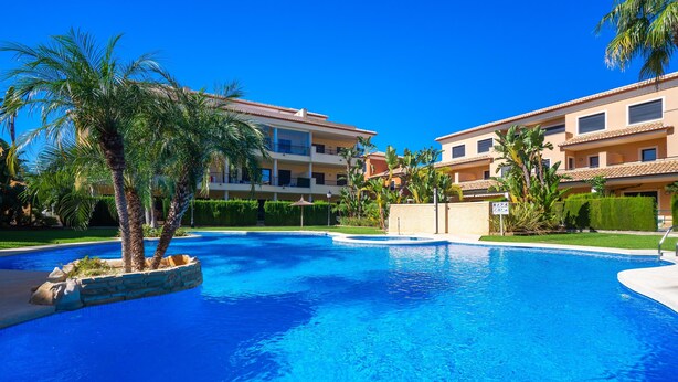 A swimming pool surrounded by palm trees and a multi-story building with balconies. - Jardines del Pla - Javea, Costa Blanca (Javea)