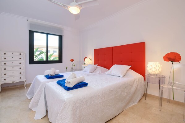 A hotel room with a large bed, a red headboard, a white dresser, and a window with a view of buildings.