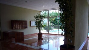 A spacious lobby with a marble floor, large potted plants, a reception desk, and a glass door leading outside. - PARAISO ESPERANTO (1 BEDROOM) (Benidorm)