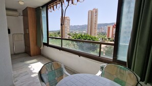 A balcony with a table and chairs, a radiator, and a view of tall buildings and greenery. - PARAISO ESPERANTO (1 BEDROOM) (Benidorm)