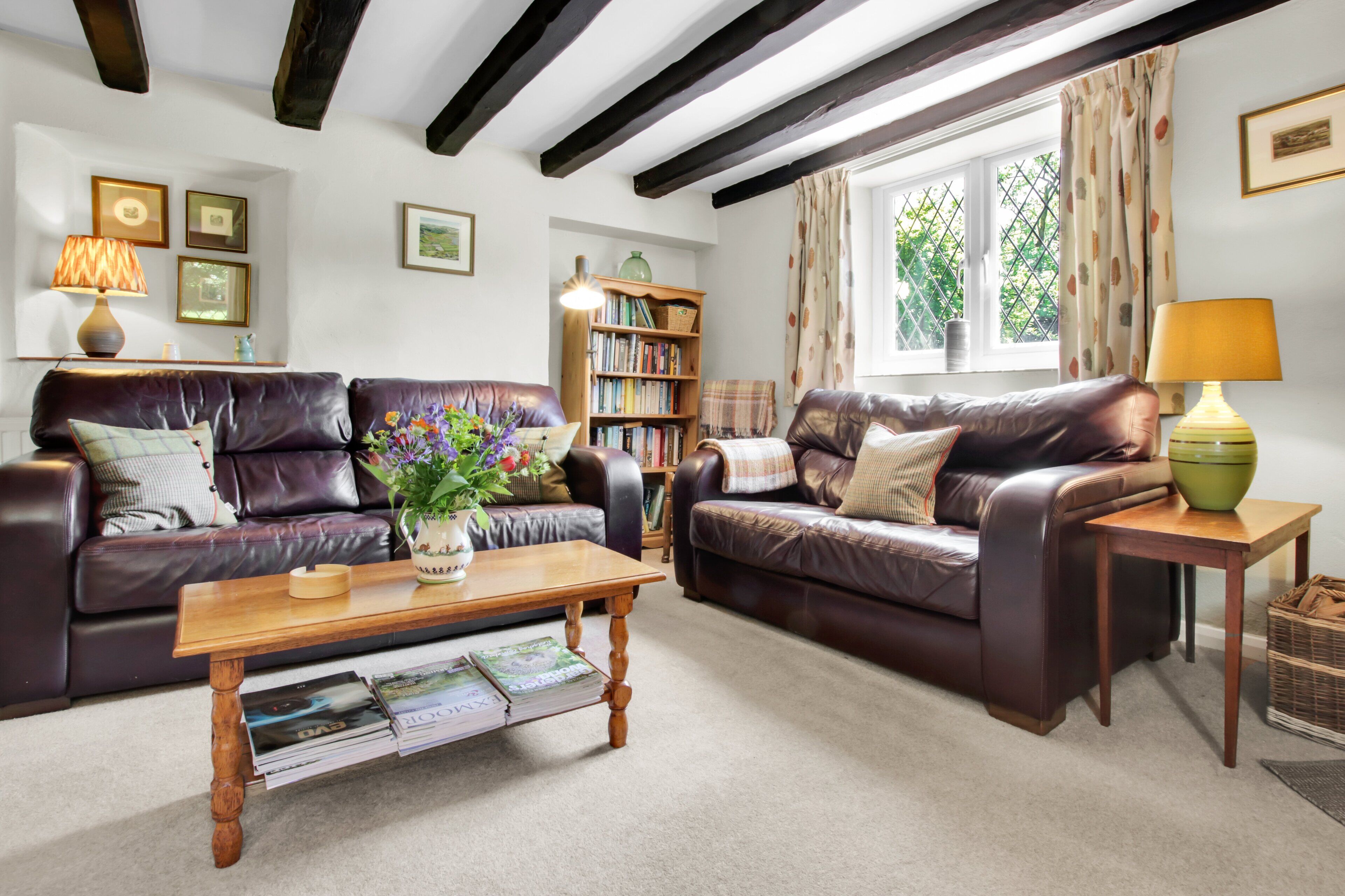 A cozy living room with two leather sofas, a wooden coffee table, and a bookshelf.