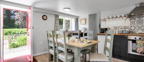 Een kleine keuken met een eettafel, stoelen, een fornuis en een raam met gordijnen.