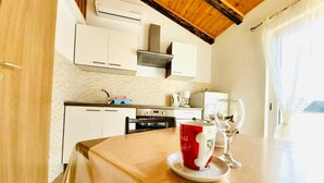 A modern kitchen with white cabinets, a stainless steel range hood, and a dining area with a table set for two. - Classic attic apartment (Supetarska Draga)