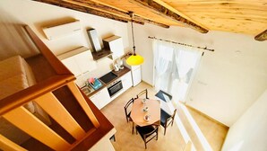 A compact kitchen with a dining area, wooden staircase, and a view of the outdoors. - Classic attic apartment (Supetarska Draga)