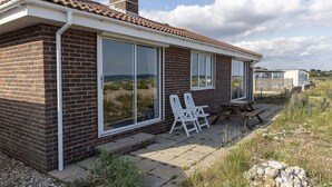 Een bakstenen huis met grote ramen, een terras met stoelen en een stenen muur.