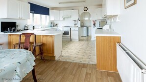 Een ruime keuken met witte kasten, een centraal eiland en een eetgedeelte met een tafel.