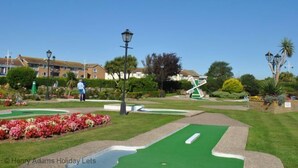 Een goed onderhouden golfbaan met geknipte gazons, een putting green en een decoratieve windmolen.