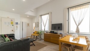 Un salon moderne avec un canapé, une table à manger et un téléviseur. On y trouve une plante et une fenêtre avec des rideaux.