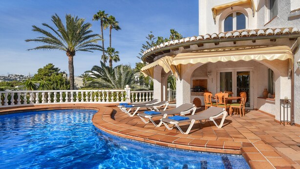A pool area with lounge chairs and a table, surrounded by a white fence and palm trees.