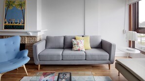 Un salón moderno con un sofá gris, un sillón azul y una mesa de centro de cristal.