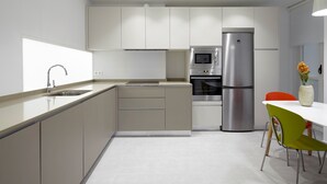 Una cocina moderna con armarios blancos, electrodomésticos de acero inoxidable y una zona de comedor con una mesa blanca y sillas verdes.