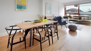 Una sala de estar moderna con una mesa de comedor de madera, sillas negras, un sofá azul y un ventanal con vistas a una colina.