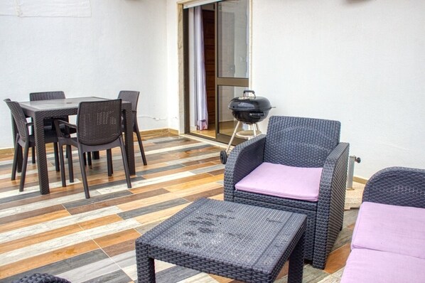 Un patio con mesa y sillas, un sofá de mimbre con cojín y una parrilla.