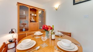 A dining area with a wooden table set for four, a cabinet with glass doors, and a wall-mounted light fixture. - 1 Bed in Ilfracombe (oc-n2052) (Berrynarbor)