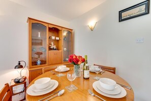 Un coin repas avec une table en bois dressée pour quatre personnes, un meuble avec des portes en verre et un luminaire fixé au mur.