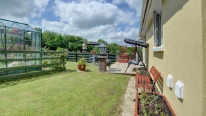 A patio with a grill, a swing, and a garden area with a fence and potted plants. - 1 Bed in Ilfracombe (oc-n2052) (Berrynarbor)