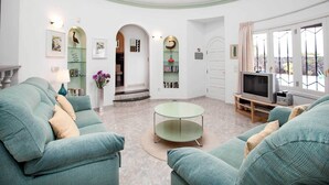 Un salon spacieux avec des canapés de couleur turquoise, une table basse en verre et un téléviseur. On y trouve également des étagères et une cheminée.