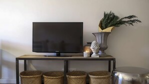 Ein Fernseher auf einer Holzkonsol mit gewebten Körben und einer dekorativen Vase mit Grünpflanzen.