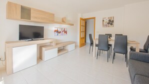 A modern living room with a flat-screen TV, wooden entertainment unit, dining table with chairs, and artwork on the walls. - Apartment Zeus - PlusHolidays (Calpe)