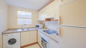 A compact kitchen with a washing machine, microwave, oven, and a refrigerator. - Apartment Zeus - PlusHolidays (Calpe)