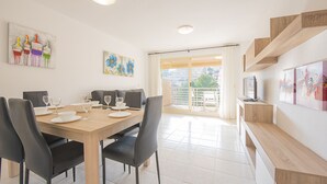 A dining area with a wooden table set for four, black chairs, and a balcony with a view of buildings. - Apartment Zeus - PlusHolidays (Calpe)