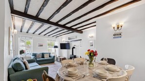 A dining area with a round table set for four, a sofa, and a television in the background.